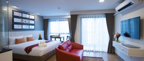 A modern hotel room with a bed, a red sofa, a TV, and a dining area with a table and chairs.