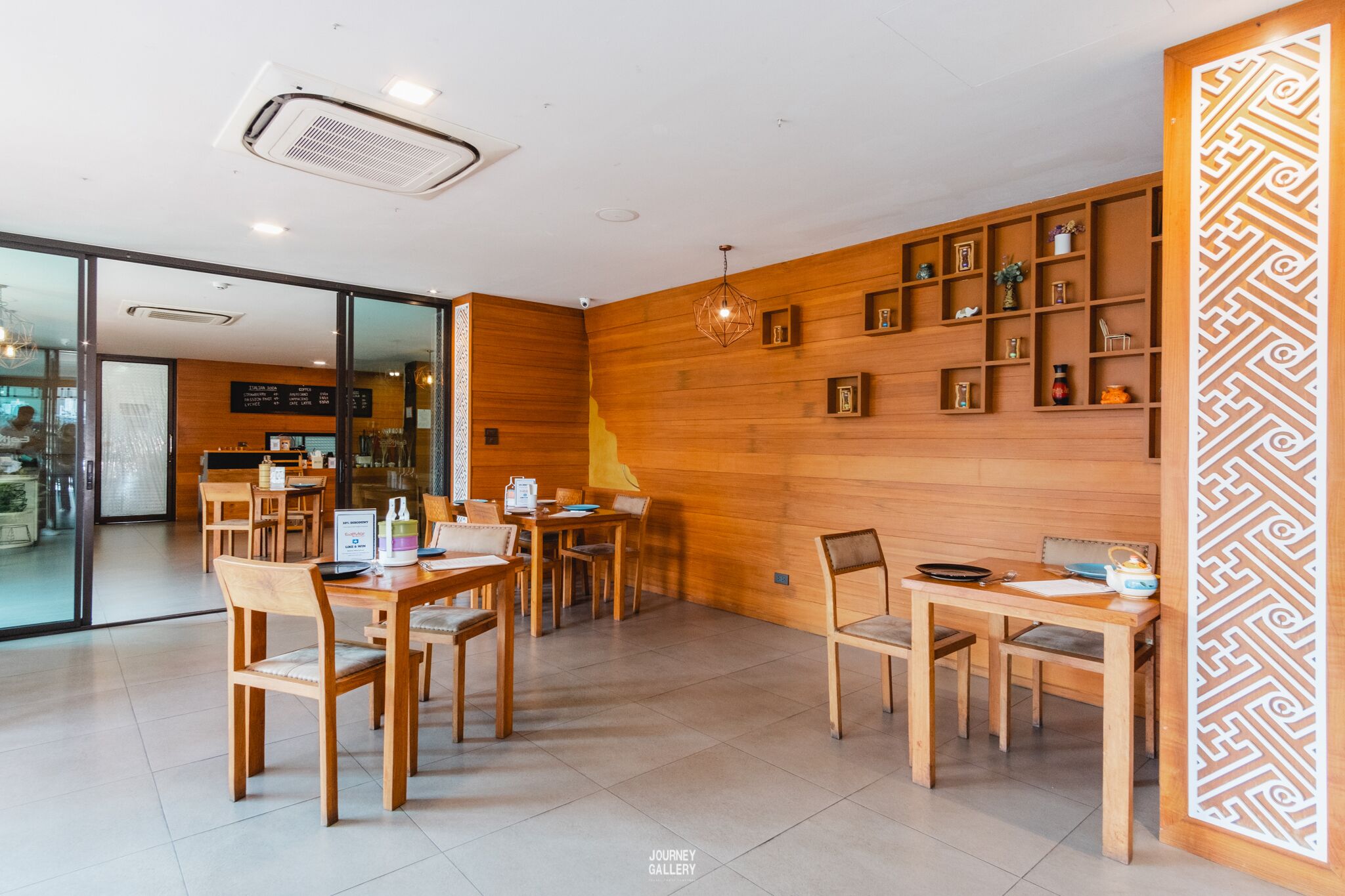 A modern interior with wooden walls, a dining area with tables and chairs, and a decorative wall panel.