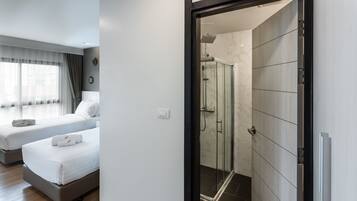 A hotel room with two beds, a shower area, and a view of the city through the window.