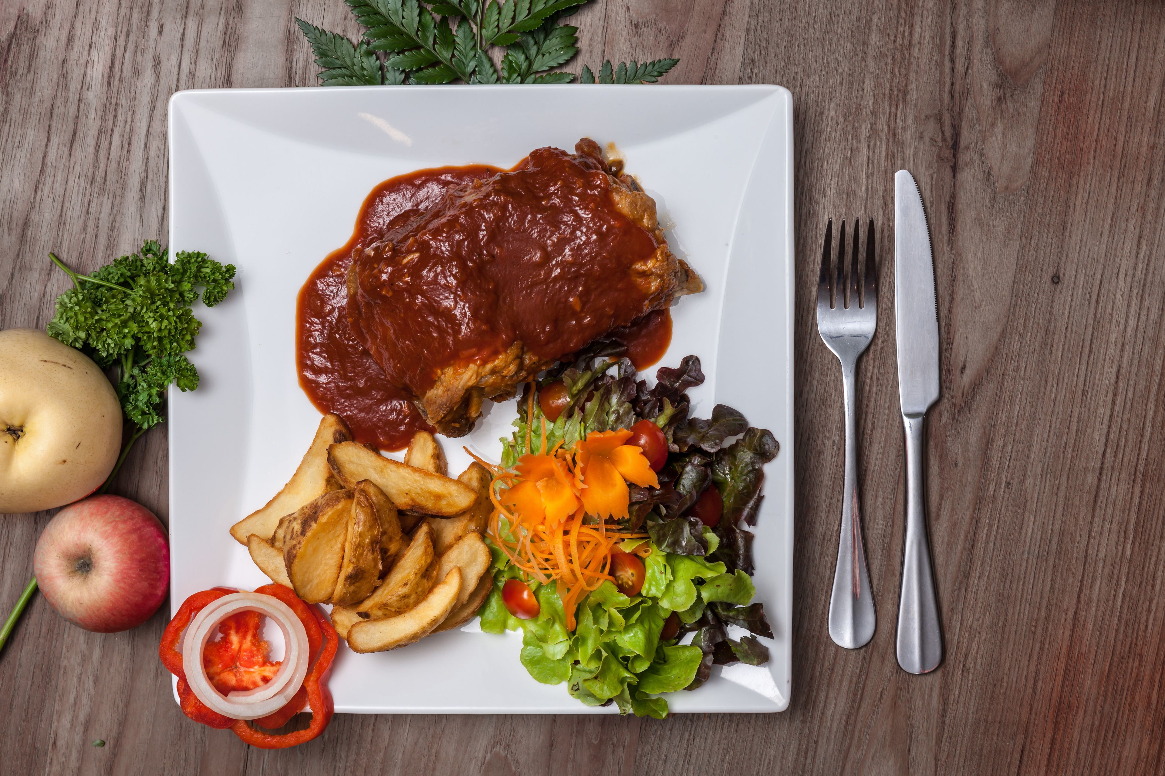 Un plato con un guiso de carne, papas fritas, ensalada y verduras sobre una mesa de madera.