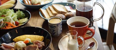 Una mesa de desayuno con diversos platos que incluyen huevos, salchichas y verduras, una cafetera y una taza de café.