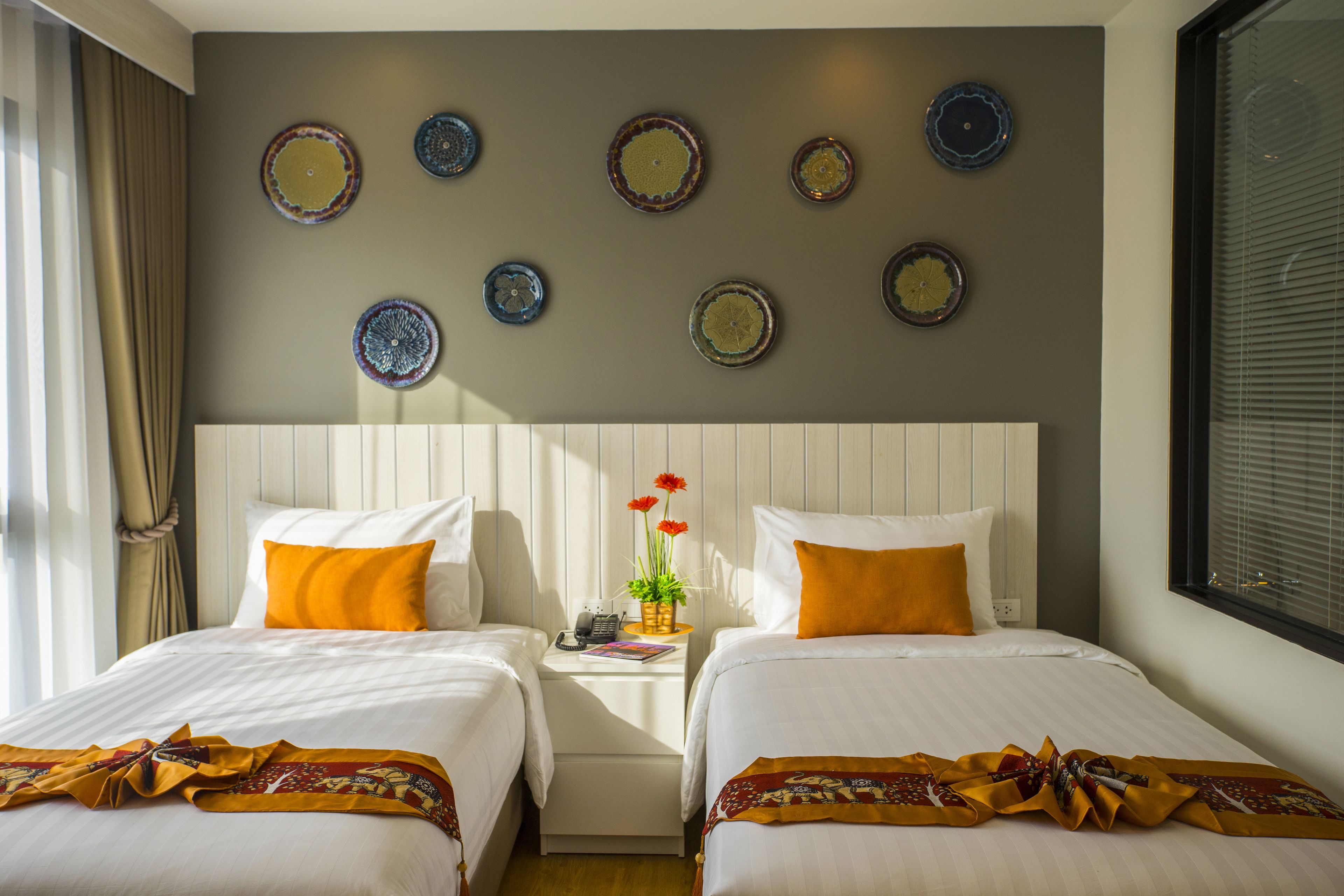 A hotel room with two beds, a nightstand, and a wall decorated with plates.