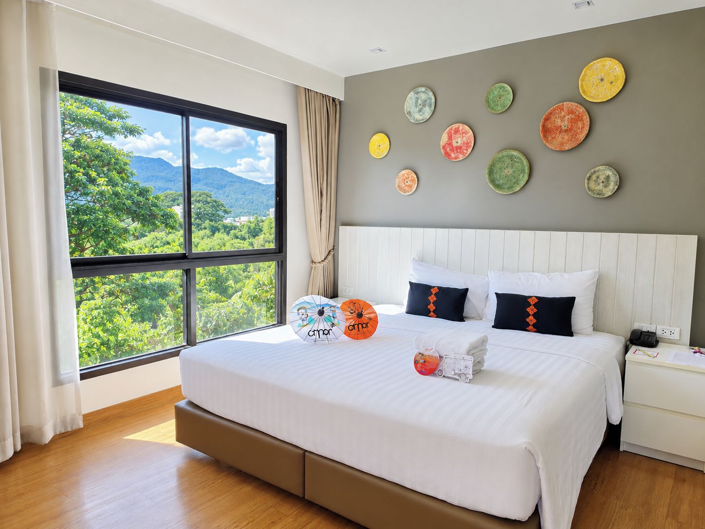 A hotel room with a large bed, a view of greenery, and decorative plates on the wall.