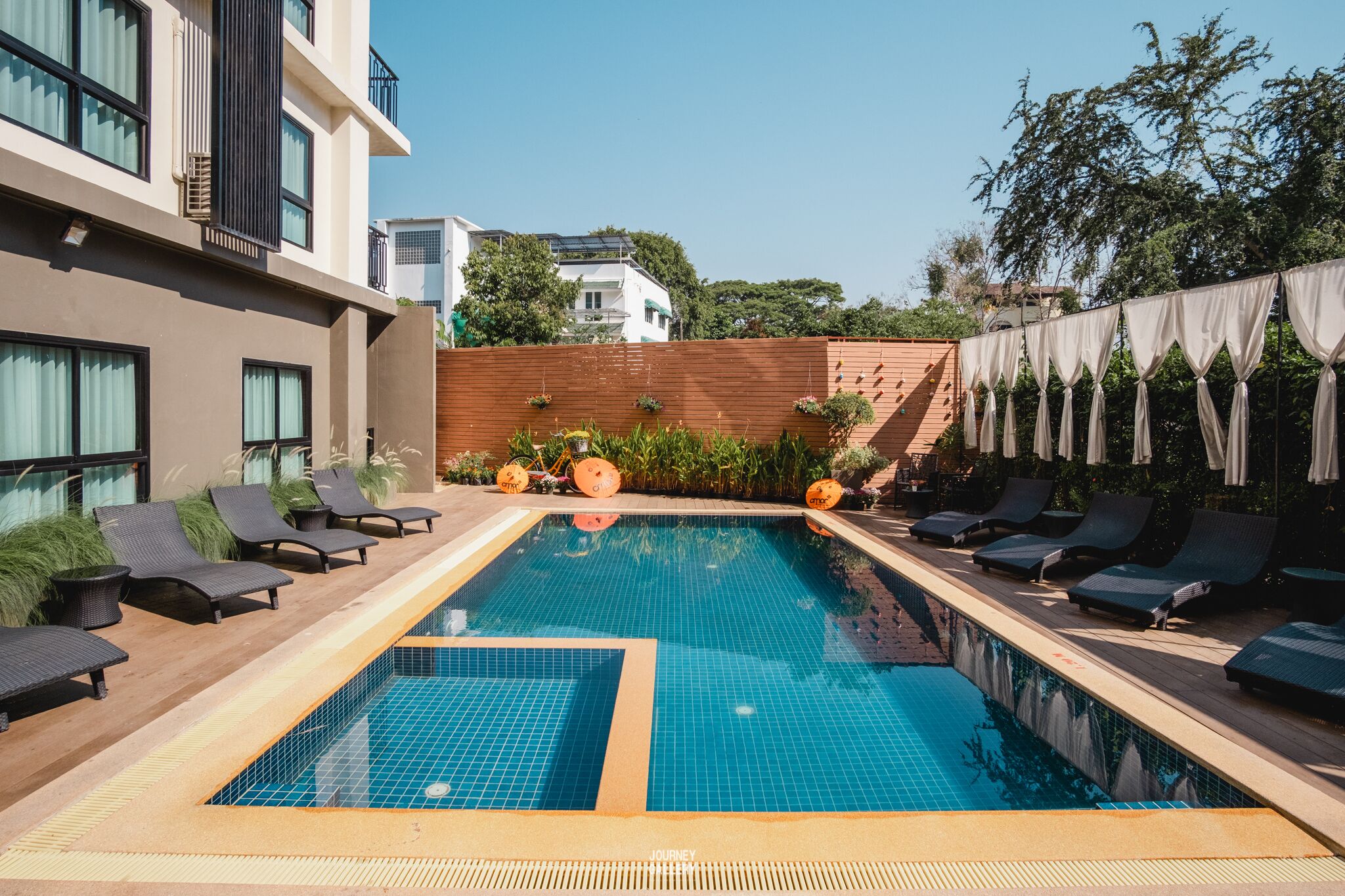 Une piscine avec des chaises longues, une terrasse en bois et un mur en briques.