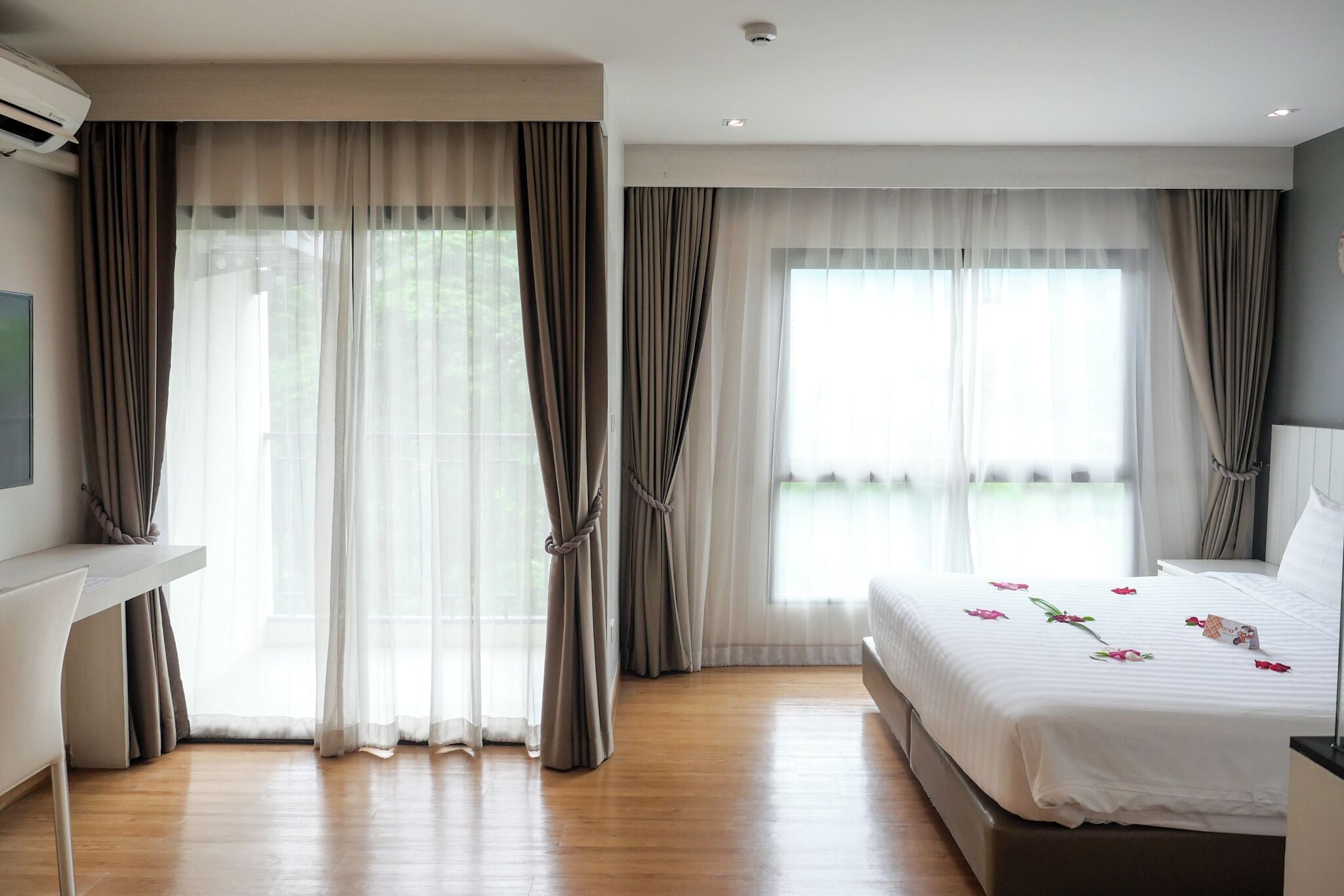 A hotel room with a bed, a desk, and large windows with curtains.