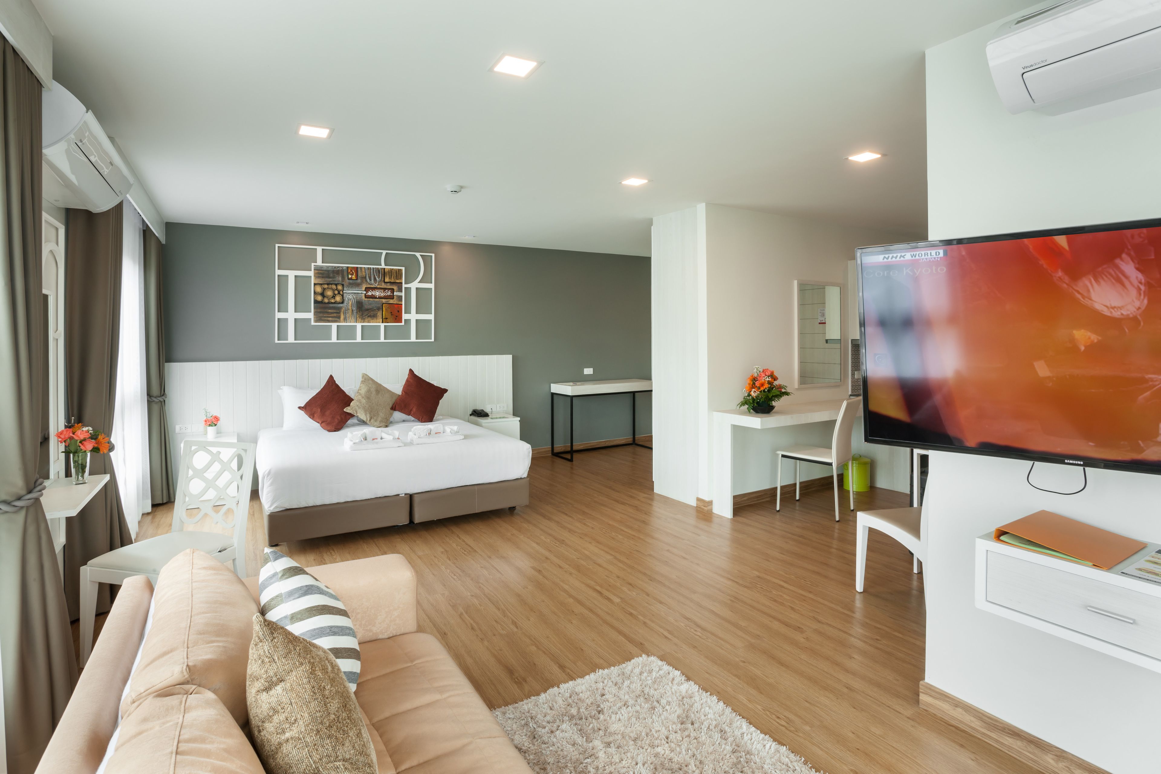 A modern hotel room with a bed, a sofa, a desk, and a TV.
