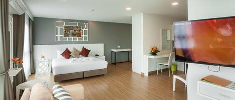 A modern hotel room with a bed, a sofa, a desk, and a TV.