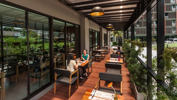 An indoor dining area with tables and chairs, large windows, and a view of greenery outside. - Cmor by Recall Hotels, Chiang Mai (Chiang Mai)
