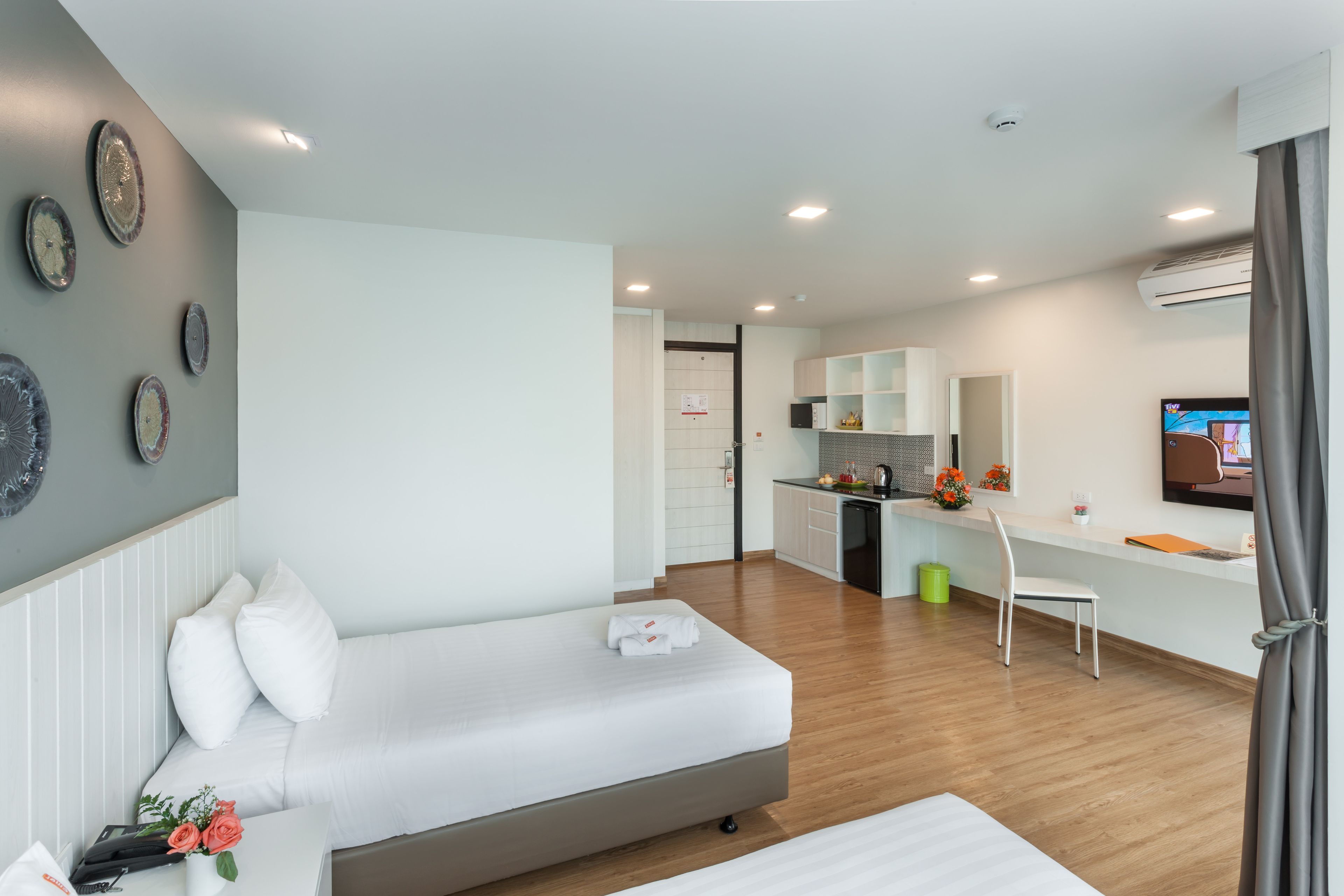 A modern hotel room with a bed, a desk, and a kitchenette.