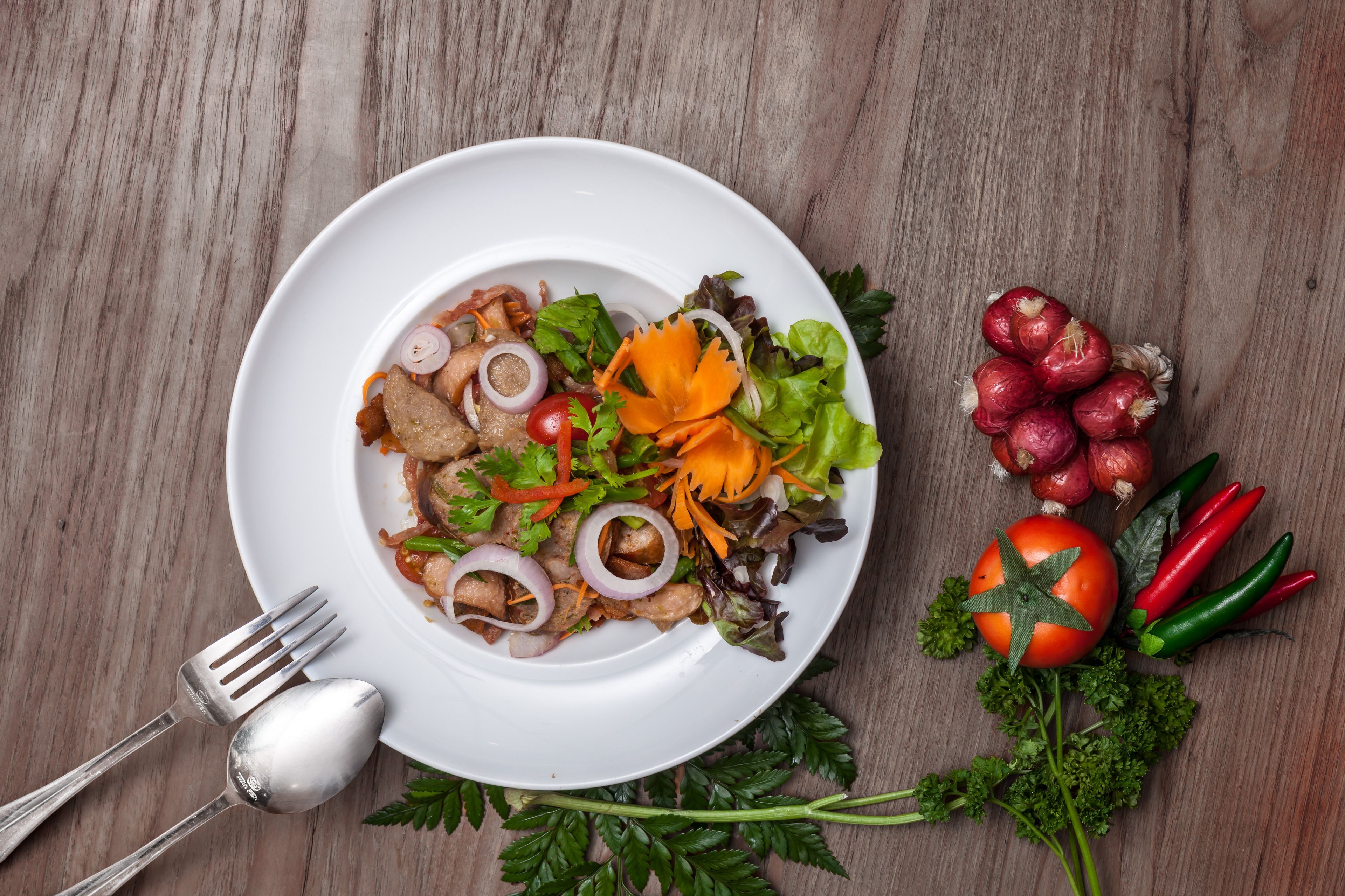 A white plate with a salad on a wooden table.