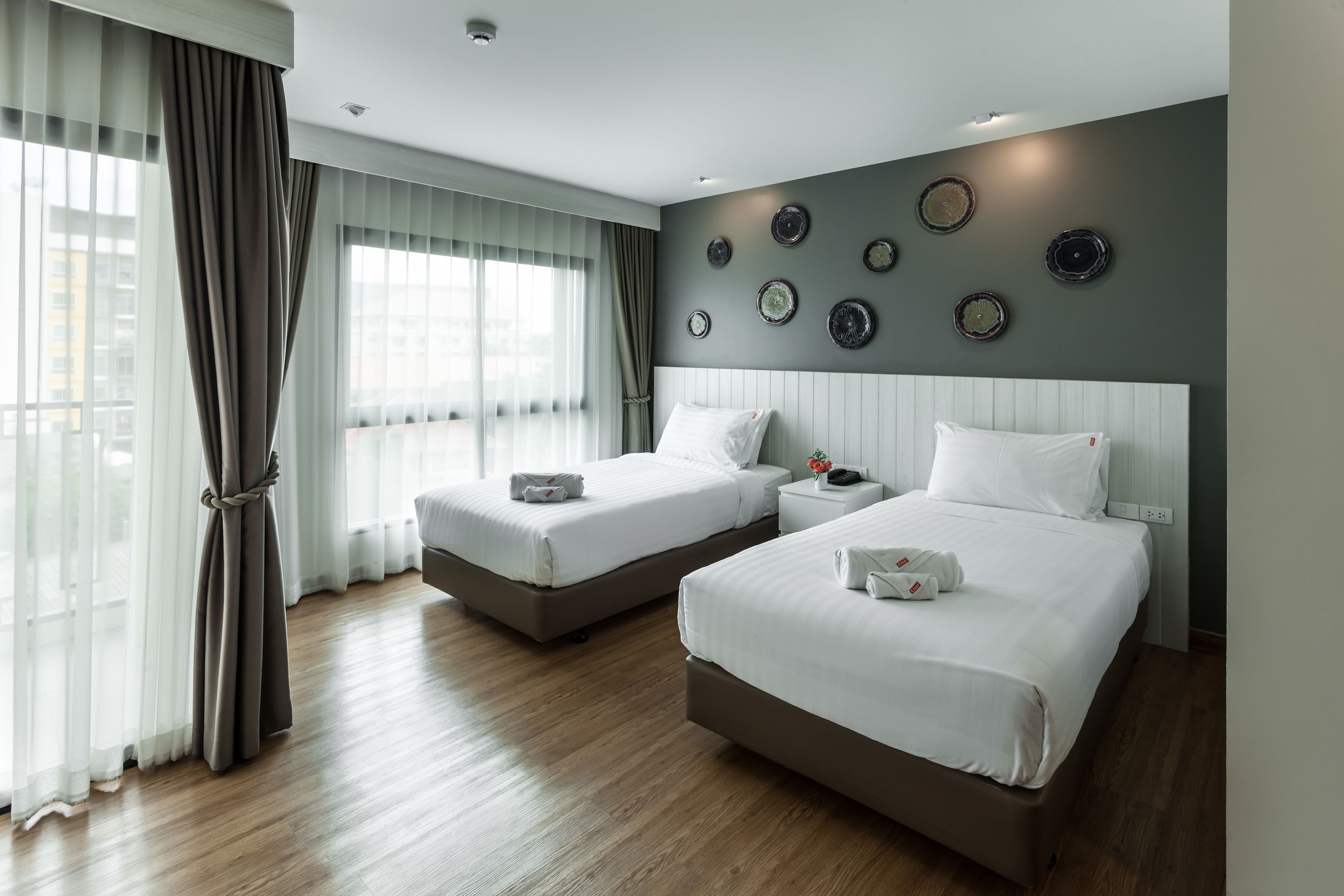 Habitación de hotel con dos camas, un ventanal con cortinas de gasa y una pared decorada con platos redondos.