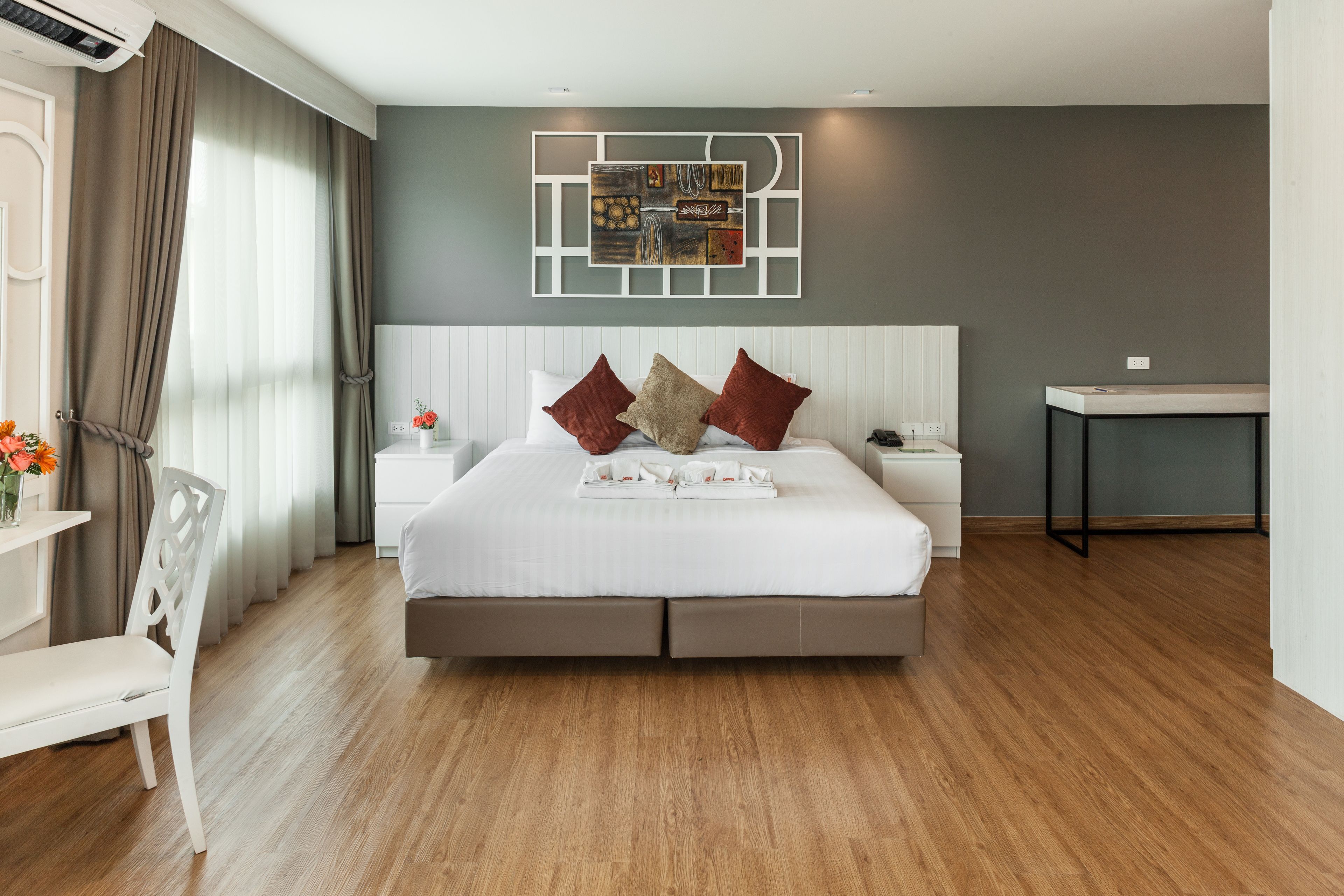 A modern bedroom with a large bed, a bedside table, a nightstand, a chair, and a wall art piece.