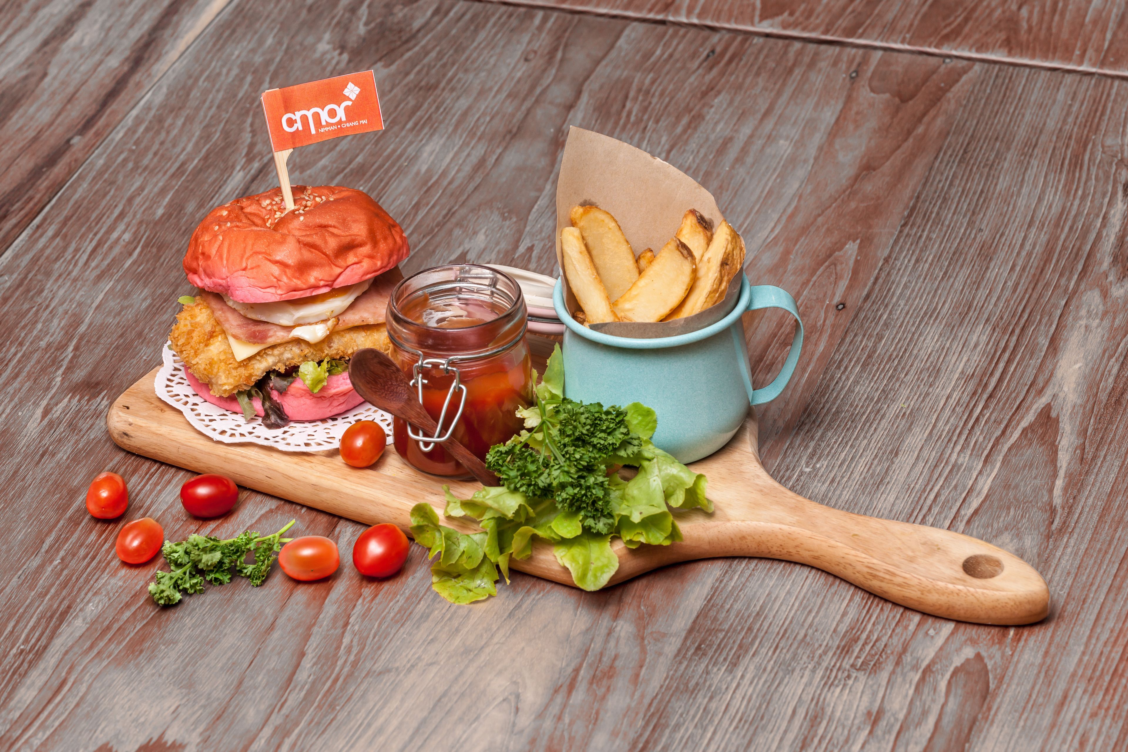 A wooden table with a sandwich, a jar of sauce, a cup of fries, and some cherry tomatoes.
