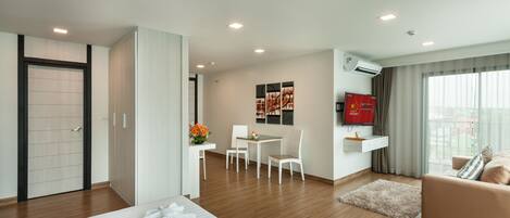 A modern hotel room with a bed, a sofa, a dining area, and a TV.