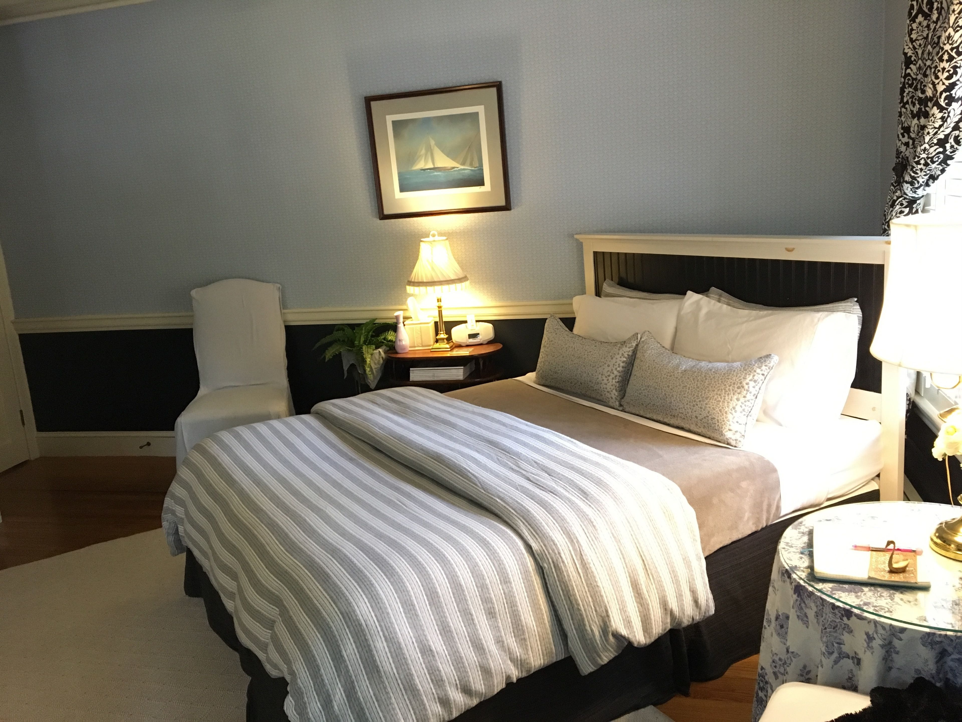 A neatly arranged bedroom with a bed, bedside table, lamp, and a framed picture on the wall.