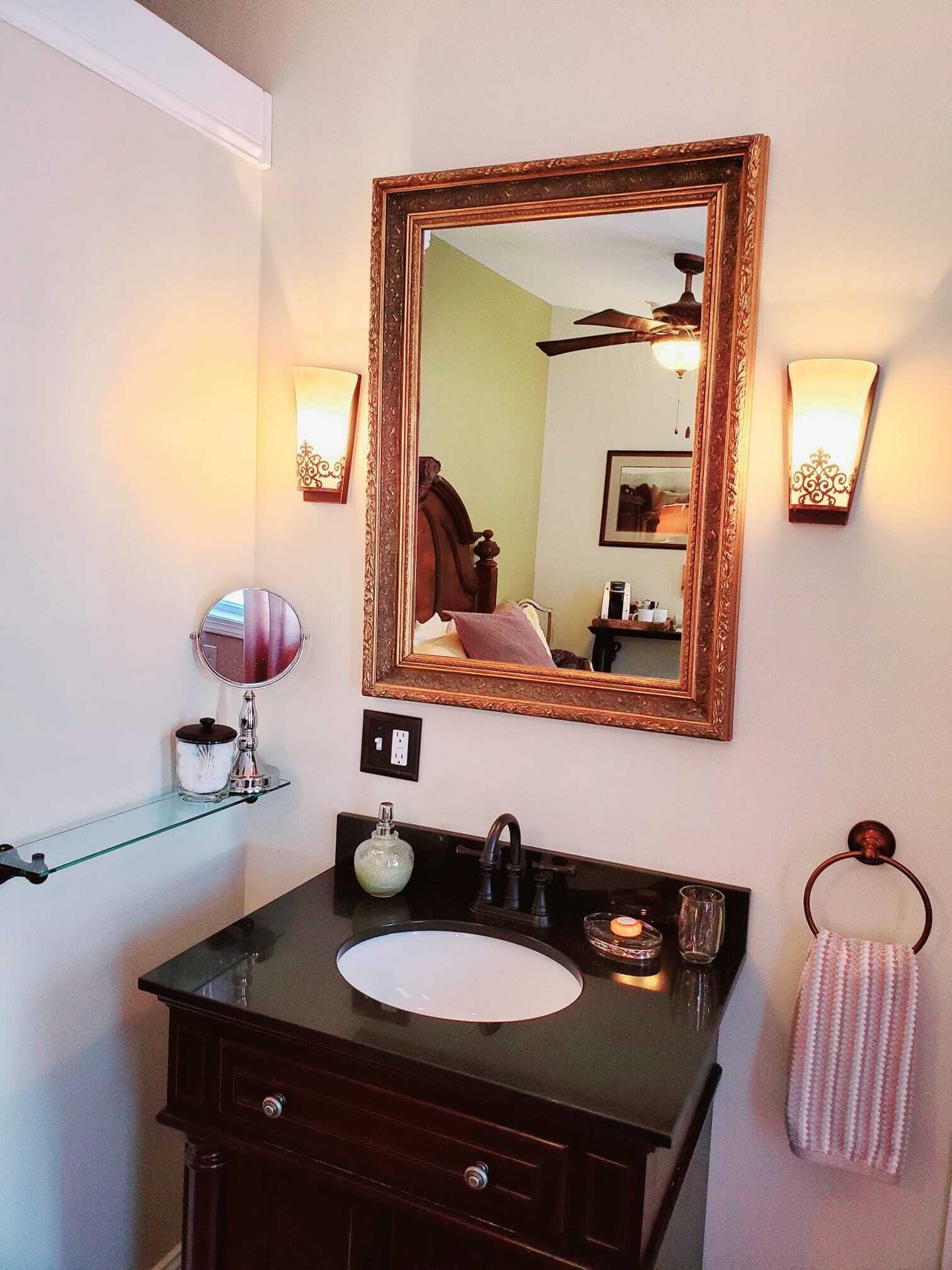 Une salle de bain avec un meuble-lavabo foncé, un miroir rond, un grand miroir et deux appliques murales.