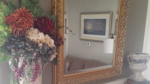 Una repisa de chimenea con un jarrón de flores, un espejo y un cuadro en la pared.