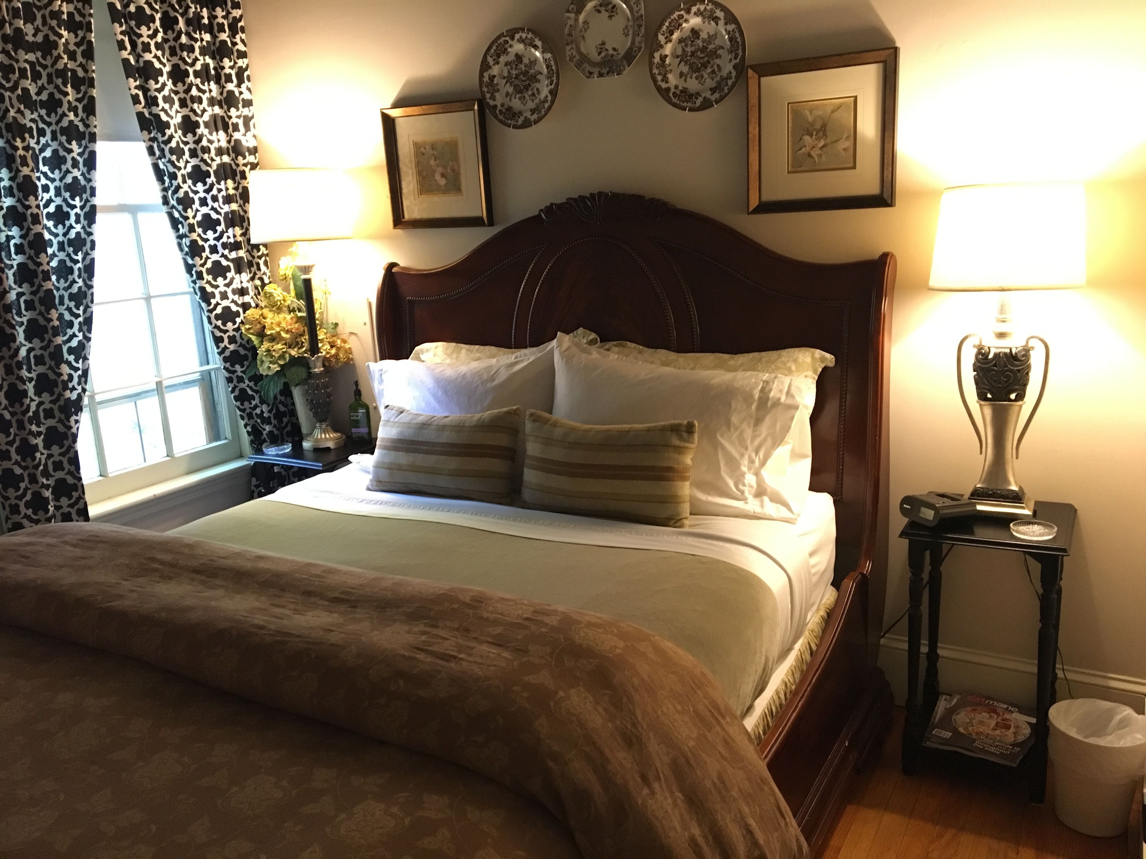 A neatly made bed with a brown bedspread, two bedside lamps, a small table with a lamp, and a trash can.