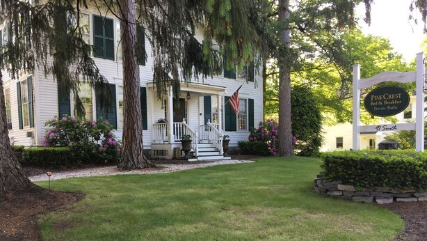 Un edificio blanco con contraventanas verdes, un porche y un letrero que indica que es Pine Crest Bed & Breakfast.