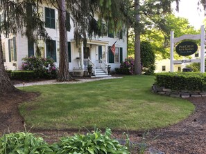 A white building with green shutters, a porch, and a sign indicating it is Pine Crest Bed & Breakfast. - PineCrest Inn (Gorham)