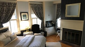 Un dormitorio con cama, escritorio, silla, chimenea y ventana con cortinas.
