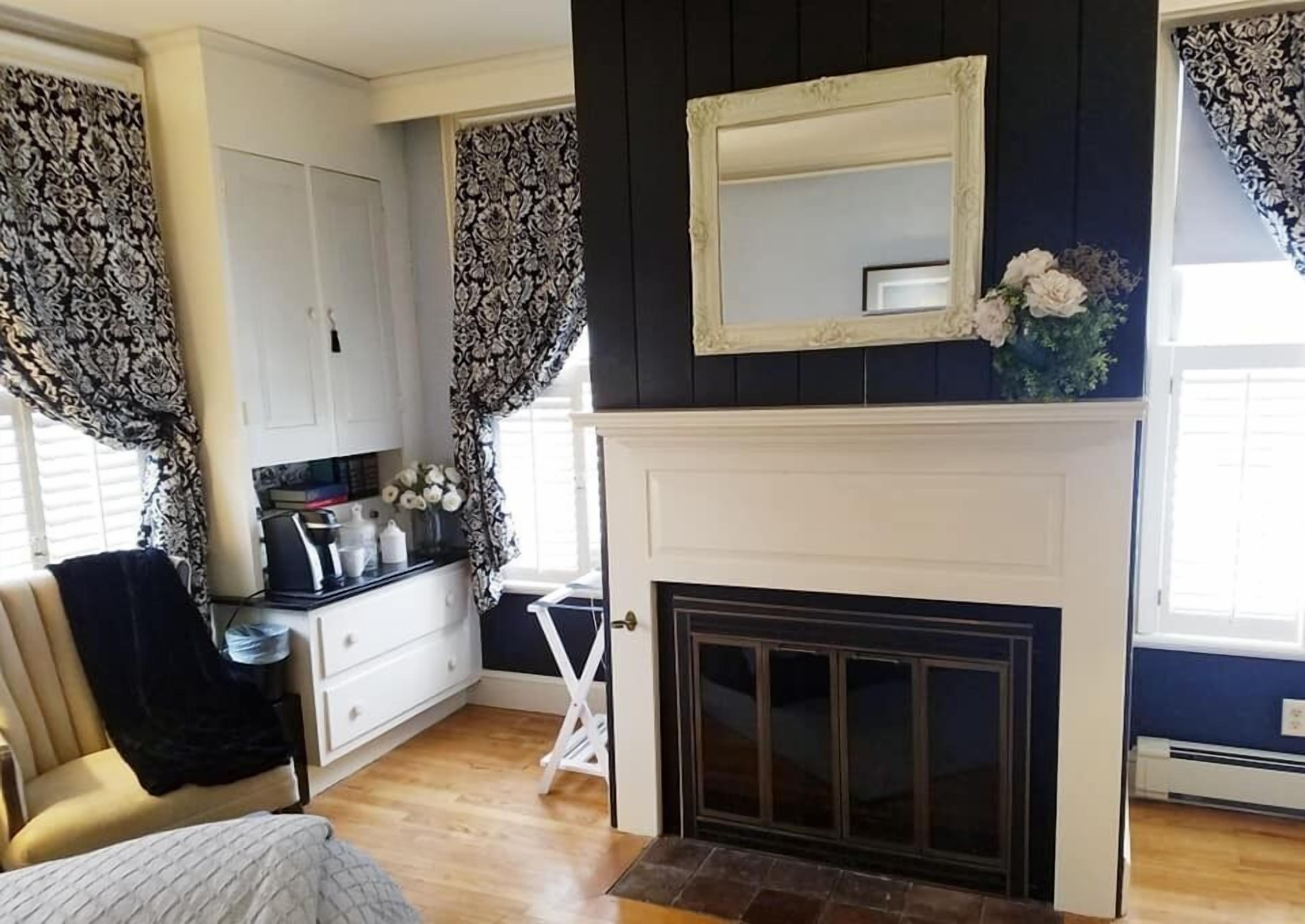 A room with a fireplace, white cabinets, a black and white patterned curtain, and a small table with books and a vase of flowers.