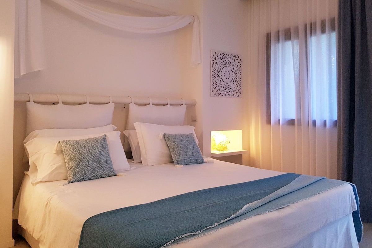 A neatly made bed with white and patterned pillows, a blue throw blanket, and a decorative wall piece.