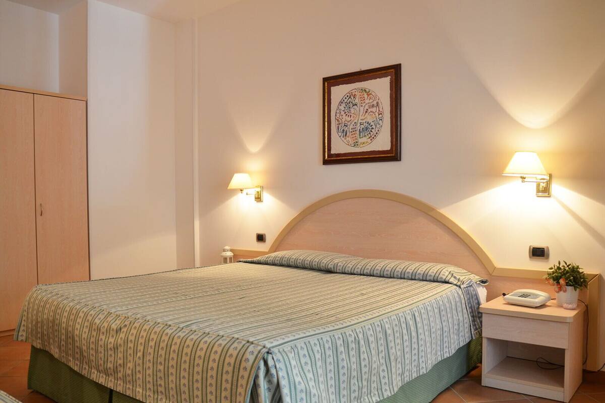 A neatly arranged bedroom with a bed, two bedside lamps, a nightstand with a phone, and a framed artwork on the wall.