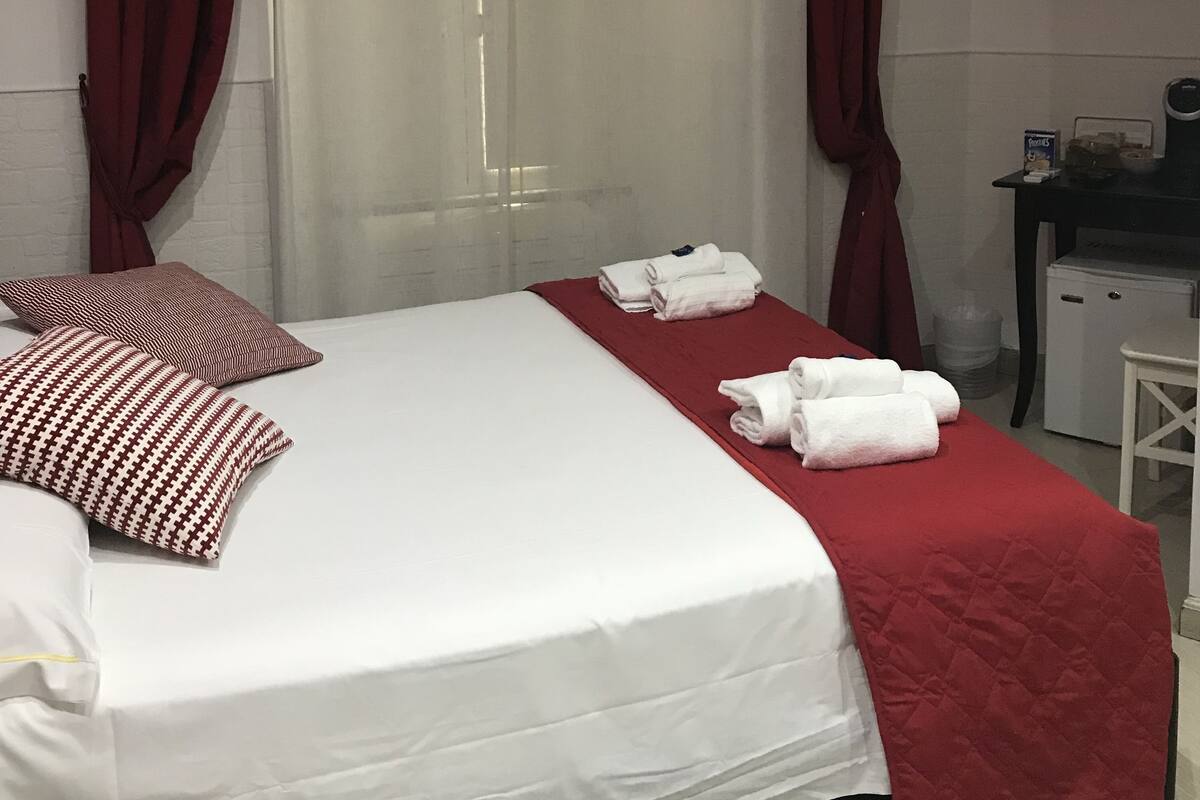 Een hotelkamer met een bed, rode gordijnen, een televisietoestel en een bureau met een koffiezetapparaat.