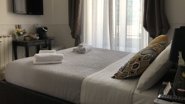 A hotel room with a bed, a desk with a coffee maker, a TV mounted on the wall, and a window with curtains. - Vatican City Holidays (Rome)