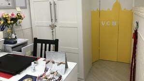A room with a desk, a chair, a vase with flowers, a clock on the wall, and a yellow door with 'VCH' on it. - Vatican City Holidays (Rome)
