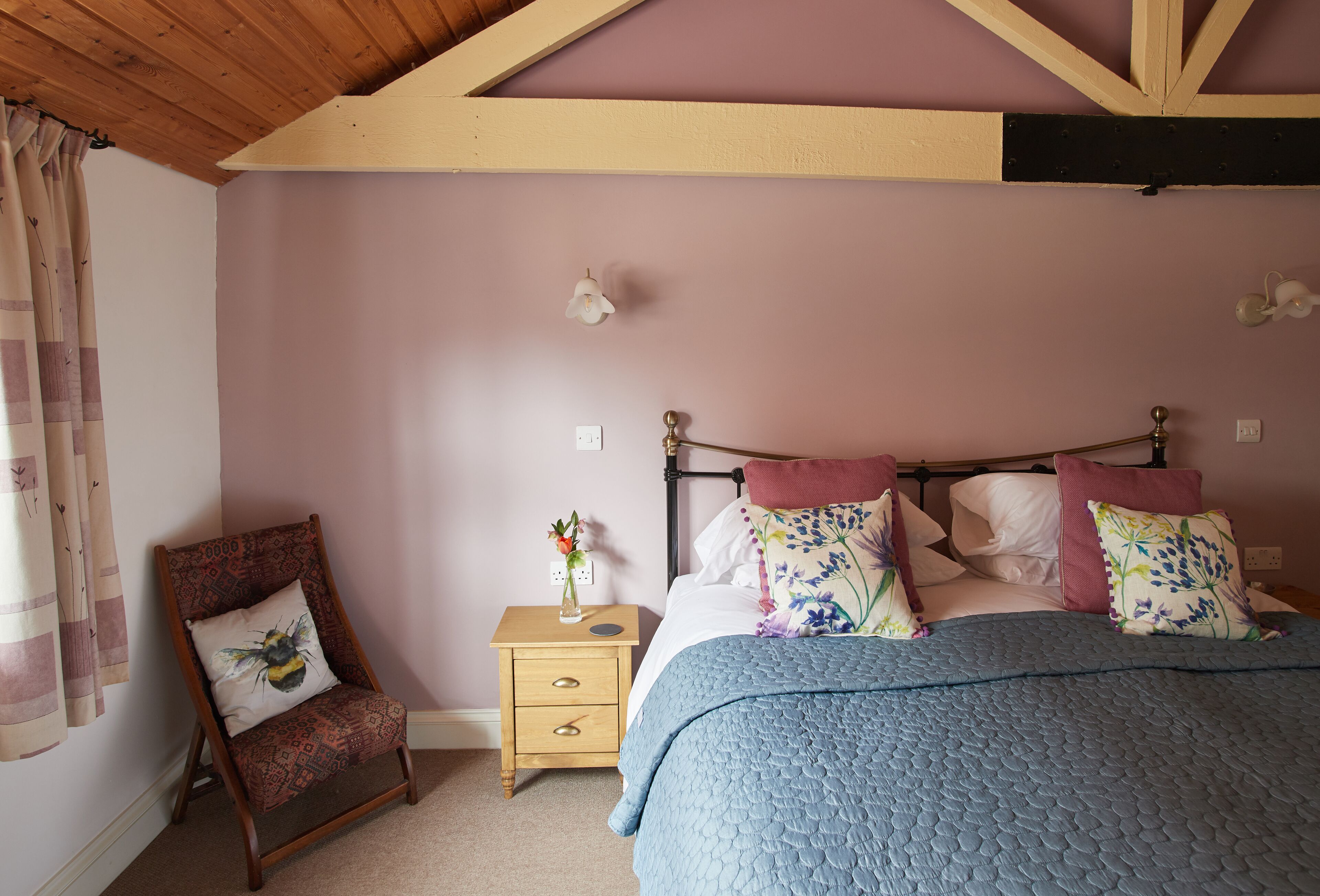 Een slaapkamer met een bed, nachtkastje, stoel en raam met gordijnen.