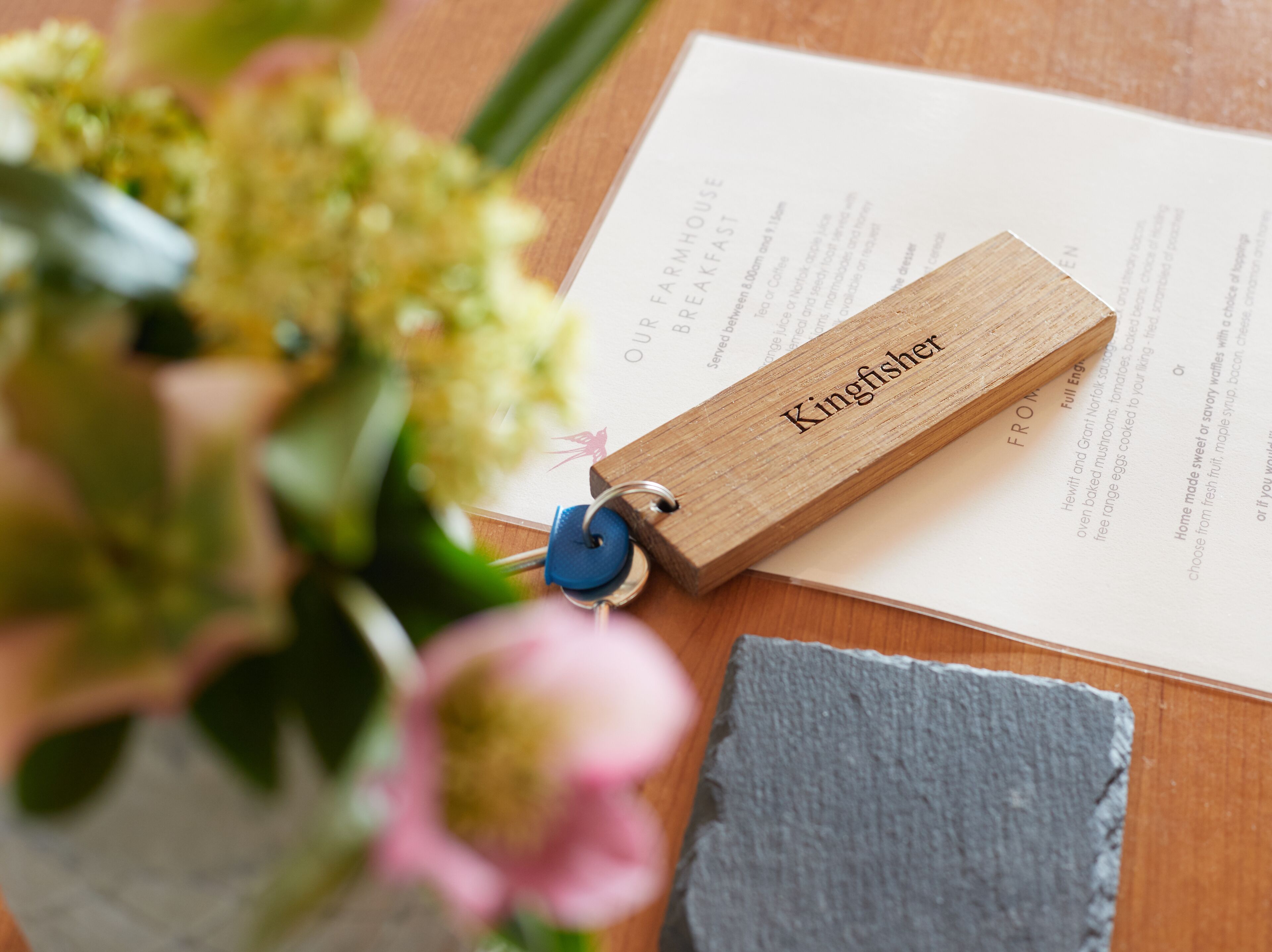 A wooden keychain with the name "Kingfisher" on a wooden surface with a menu or document.