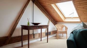 Une pièce avec un plafond en pente, une table en bois dotée de tiroirs, une chaise en osier et un lit.