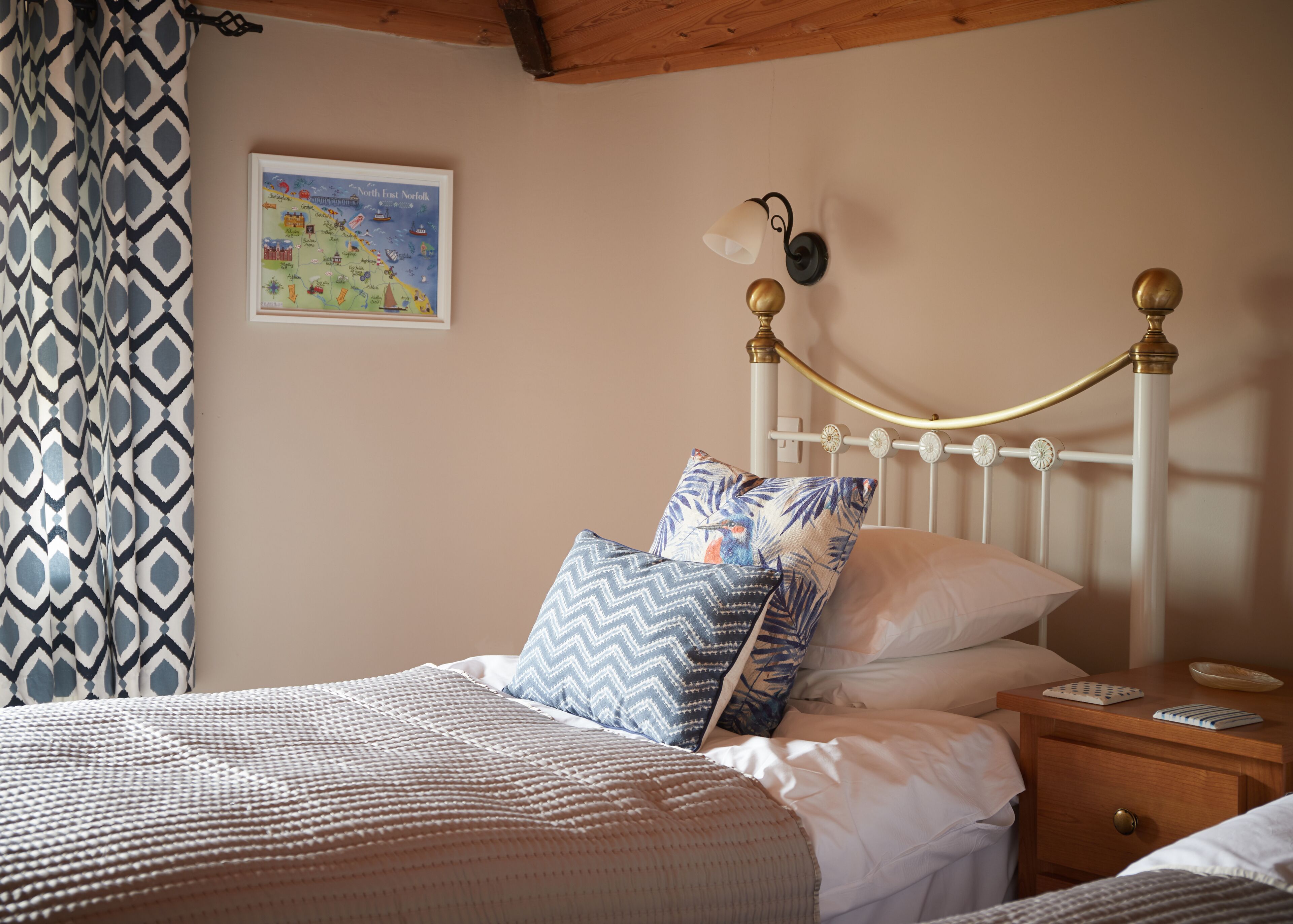 A neatly made bed with patterned pillows, a bedside table with a remote control, and a wall map.