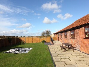 A backyard with a checkered lawn, a picnic table, and a brick building with a tiled roof.