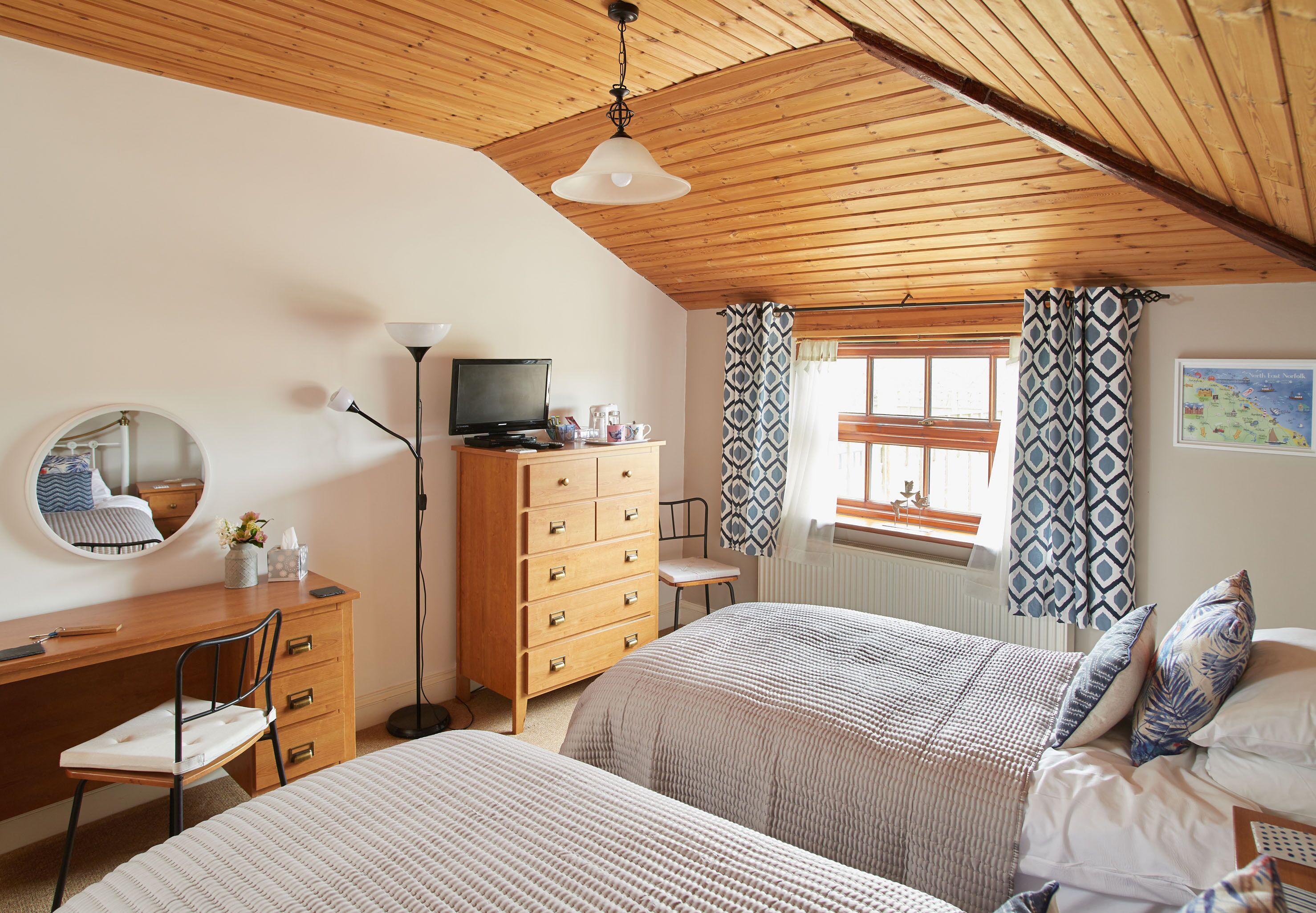 Un dormitorio con techo de madera, un escritorio con silla, un aparador y dos camas.