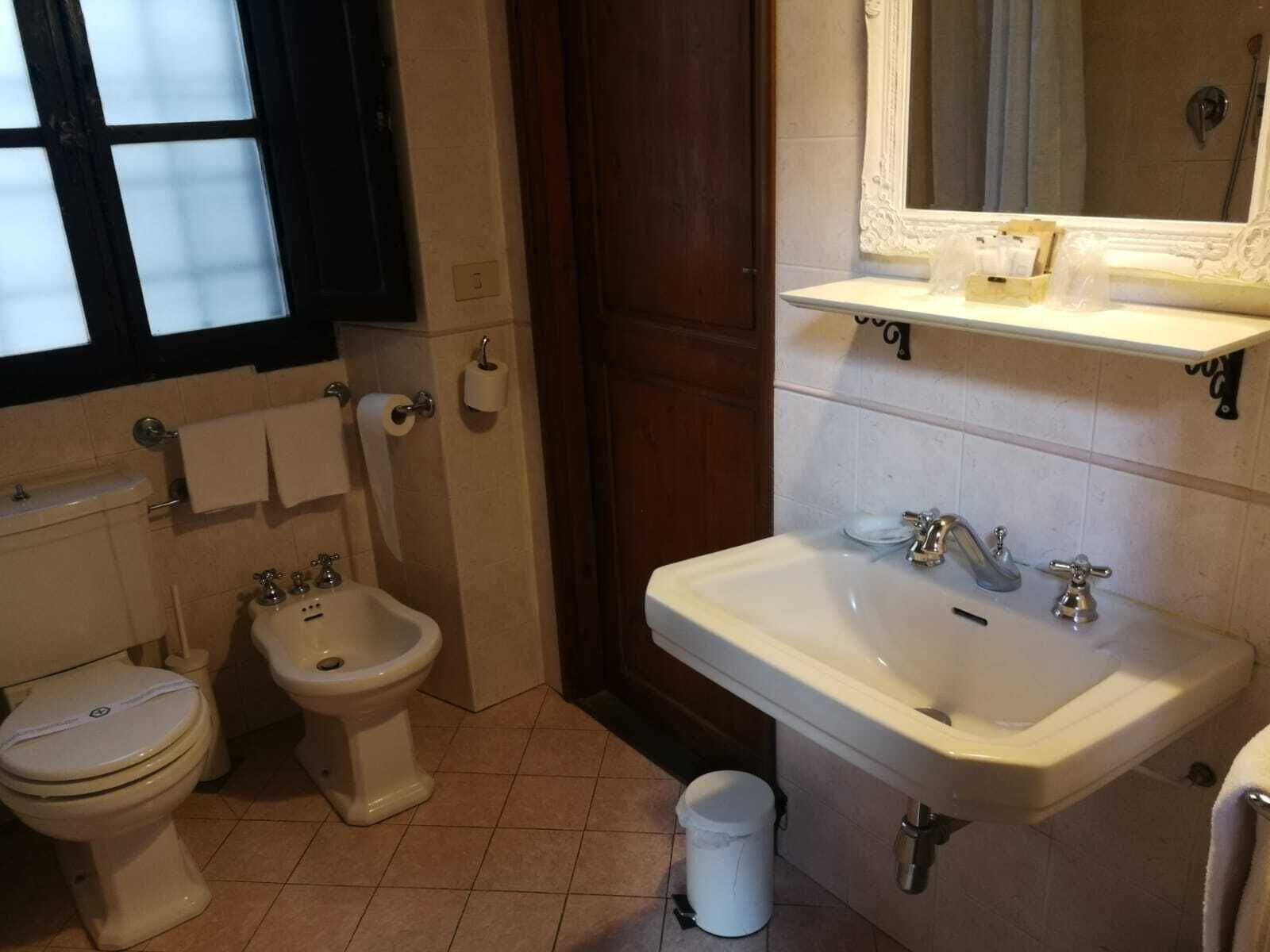 A bathroom with a toilet, bidet, sink, and mirror.