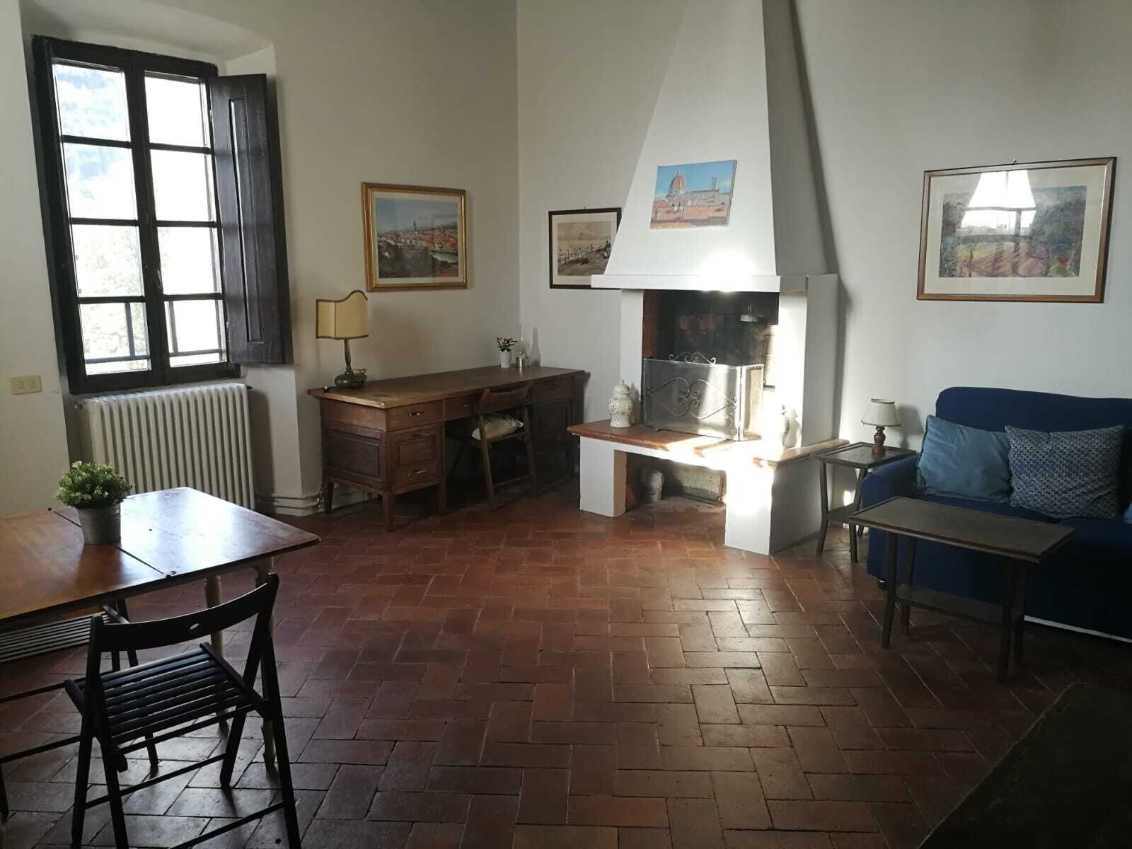 A cozy living room with a fireplace, a dining table, a sofa, and a window with blinds.
