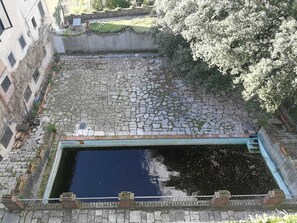 A courtyard with a stone floor, a small pool, and a bridge.