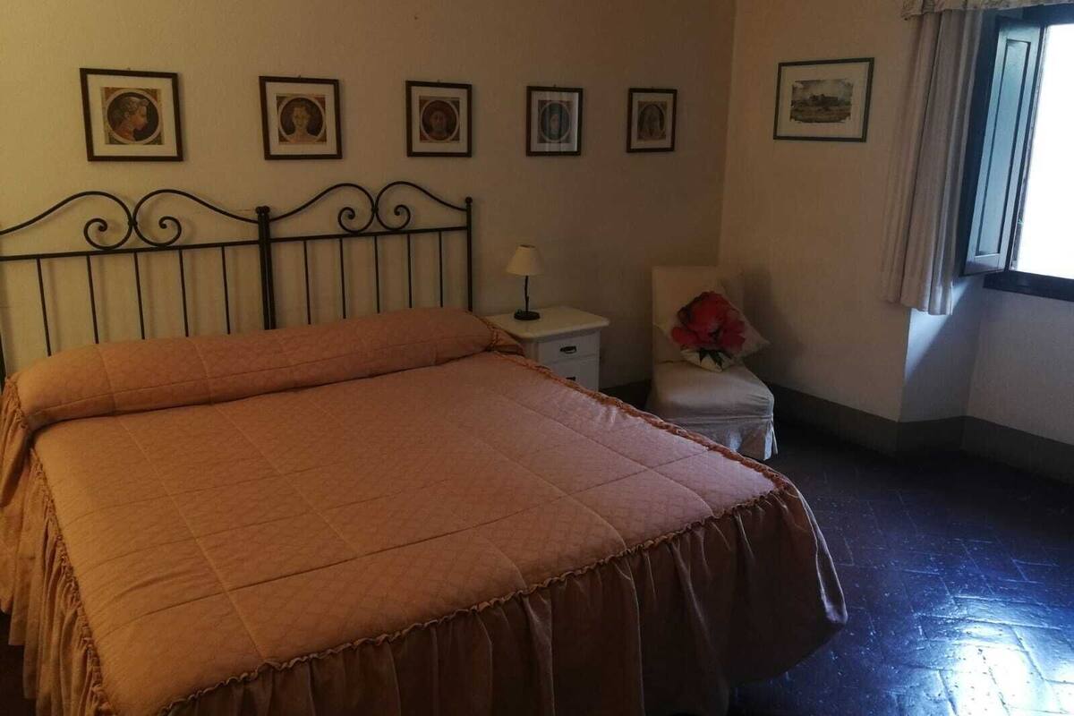 Une chambre à coucher avec un lit, une table de chevet, une chaise et une fenêtre avec des rideaux.