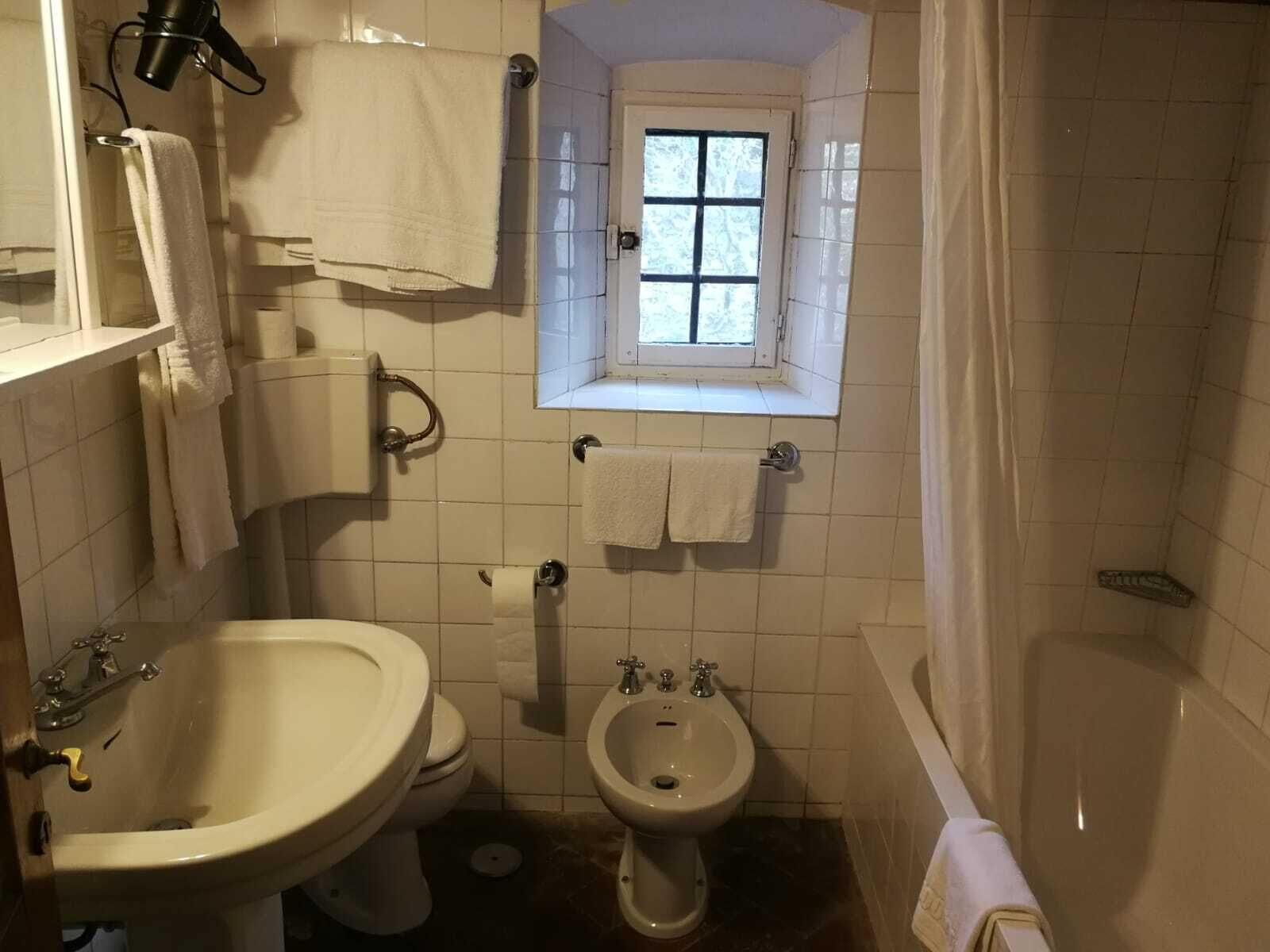 Ett litet badrum med handfat, toalett, bidé och ett litet fönster.