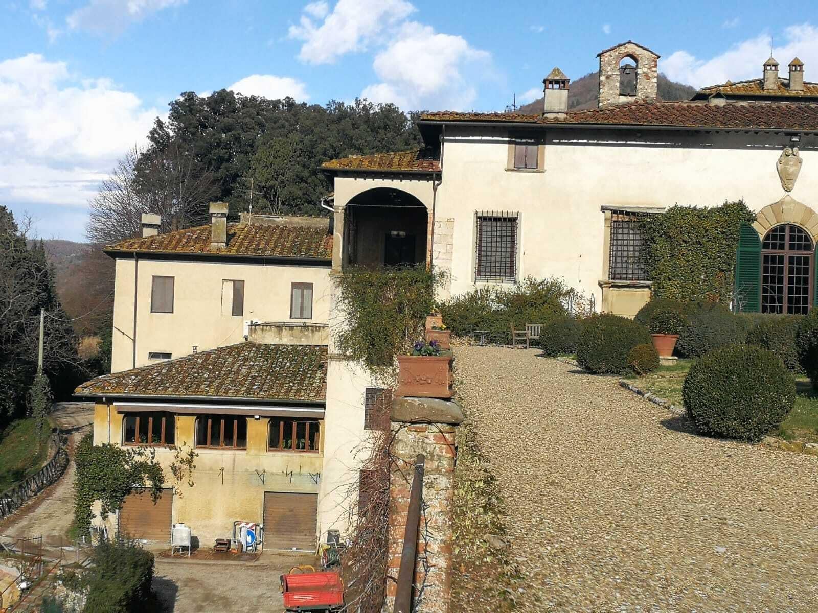 Un bâtiment traditionnel, avec un chemin pavé menant à une entrée fermée par un portail, entouré de verdure et adossé à un paysage montagneux.