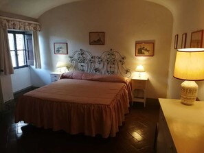 A bedroom with a bed, two bedside tables with lamps, a window with curtains, and wall-mounted artwork.