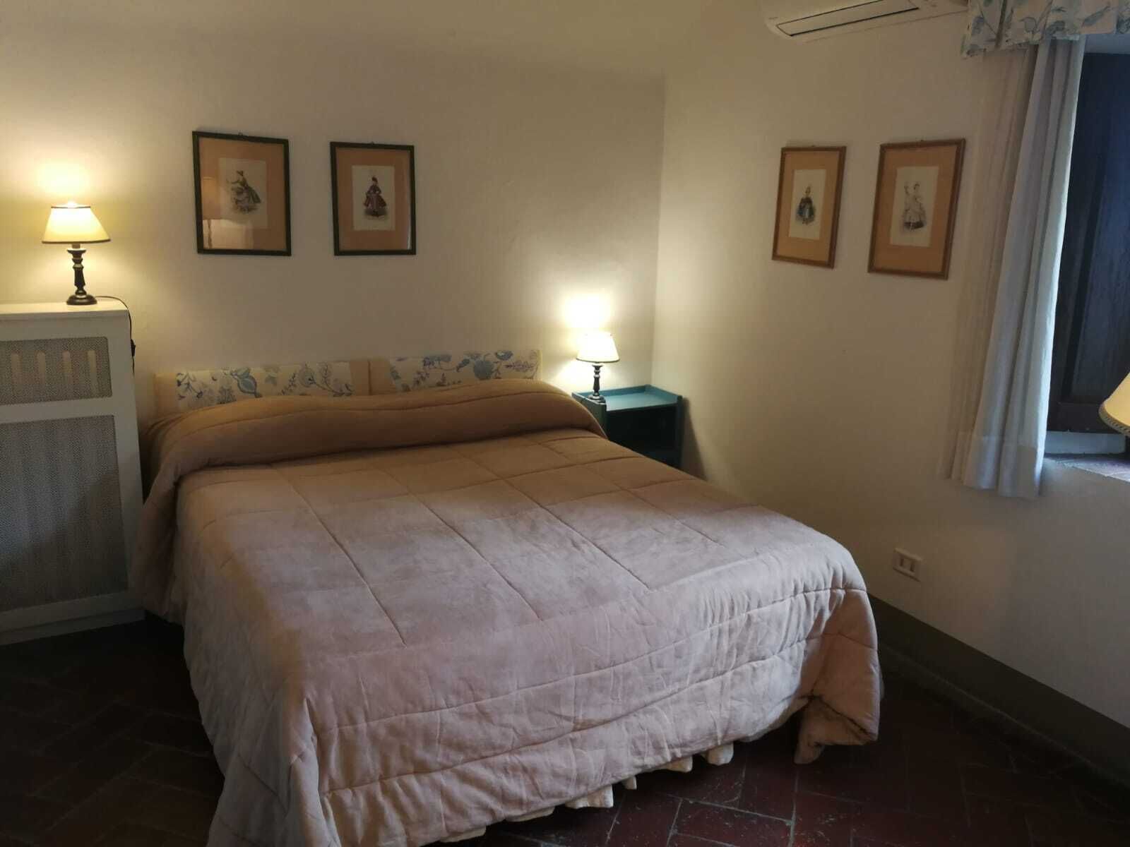A bedroom with a bed, two bedside tables, a radiator, and framed pictures on the wall.