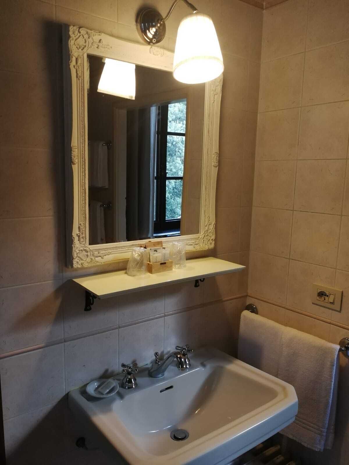 Une salle de bain avec un lavabo blanc, un miroir doté d’un cadre orné et une étagère contenant des articles de toilette.