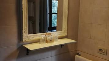Une salle de bain avec un lavabo blanc, un miroir doté d’un cadre orné et une étagère contenant des articles de toilette.