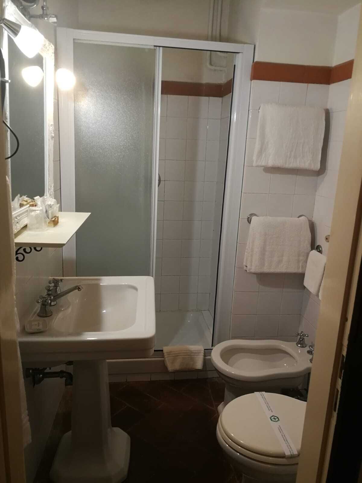 A bathroom with a shower, two sinks, a toilet, and a mirror with lights.