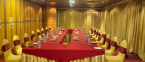 Un salón de conferencias con una larga mesa, sillas amarillas adornadas con cintas rojas y un mantel rojo.