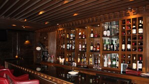 A bar area with wooden shelves stocked with various bottles, a polished bar counter, and red leather bar chairs. - Druk Hotel (Thimphu)